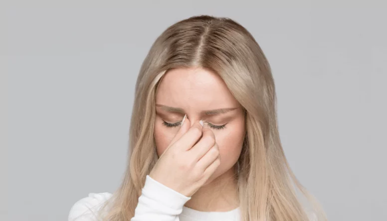 Kobieta cierpiąca na ból głowy przy schylaniu, trzyma się za skroń – możliwe, że jest to objaw ostrego zapalenia zatok przynosowych