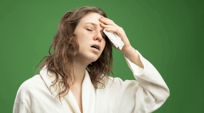Kobieta w szlafroku trzyma się za głowę z chusteczką w ręku, cierpi na gorączkę podczas zakażenia wirusowego