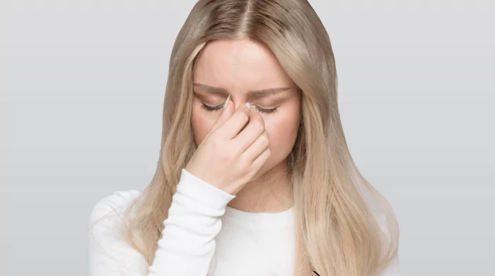 Kobieta cierpiąca na ból głowy przy schylaniu, trzyma się za skroń – możliwe, że jest to objaw ostrego zapalenia zatok przynosowych