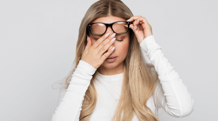 Kobieta podnosi okulary na czoło, aby rozmasować czoło dłonią, cierpi na ból głowy